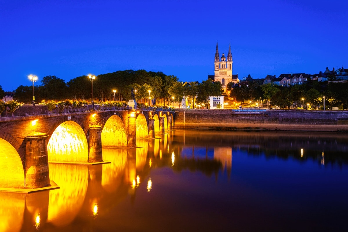 Le pont de Verdun illuminé à l’heure bleue, plus ancien passage d’une rive à l’autre de la Maine, et ses arches de pierre reflétées dans la rivière, avec la cathédrale Saint-Maurice et ses flèches dominant la Cité, le plus ancien quartier d’Angers, dans le département de Maine-et-Loire, en région Pays de la Loire.