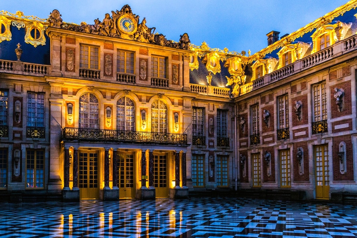 Cour de Marbre du château de Versailles à la tombée de la nuit, avec son pavement de marbre noir et blanc, son balcon sur colonnes jumelées de marbre rouge, son horloge entourée du groupe sculpté de Mars et Hercule, ses bustes de marbre et ses toitures aux faîtages dorés, au cœur du château inscrit au patrimoine mondial de l’UNESCO, dans le département des Yvelines, en région Île-de-France. Cour de Marbre du château de Versailles à la tombée de la nuit, avec son pavement de marbre noir et blanc, son balcon sur colonnes jumelées de marbre rouge, son horloge entourée du groupe sculpté de Mars et Hercule, ses bustes de marbre et ses toitures aux faîtages dorés, au cœur du château inscrit au patrimoine mondial de l’UNESCO, dans le département des Yvelines, en région Île-de-France.